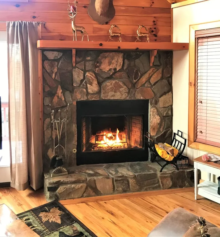 Stone fireplace with a burning fire, wood mantel and deer figurines in the cabin living room